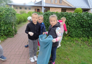 dwie dziewczynki i chłopiec stoją w koło niebieskiego worka na śmieci